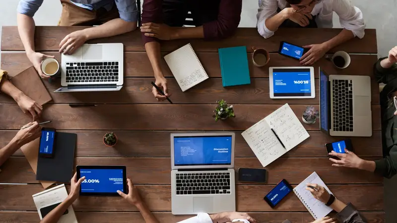Équipe au travail autour d'une table couverte d'ordinateurs et de carnets
