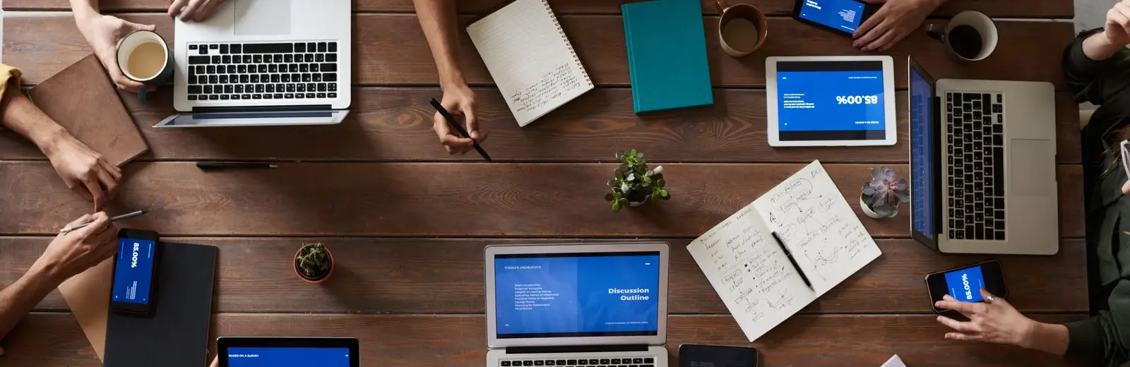 Équipe au travail autour d'une grande table couverte d'ordinateurs, de tablettes et de carnets