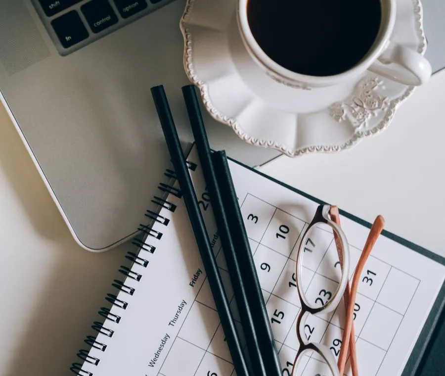Un agenda ouvert, une tasse de café et un ordinateur portable posés sur un bureau